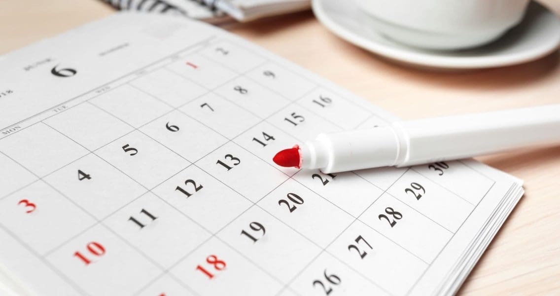 A calendar for June shows marked dates with a red pen beside a cup of coffee on a desk.